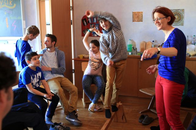 Bewegung im Klassenzimmer: Ein Junge balanciert auf einer Stange mit Kindern drumherum und Lehrerin, die lächelt