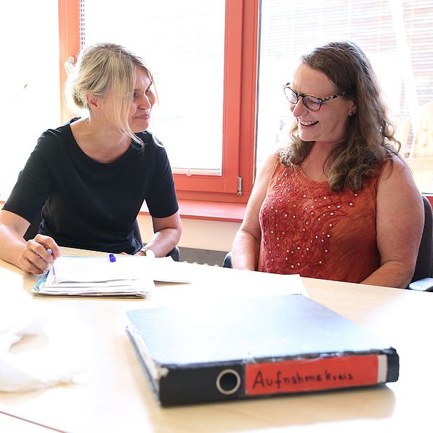 Beratungsgespräch zwischen Lehrerin und lächelnder Mutter am Tisch in unserem Sekretariat