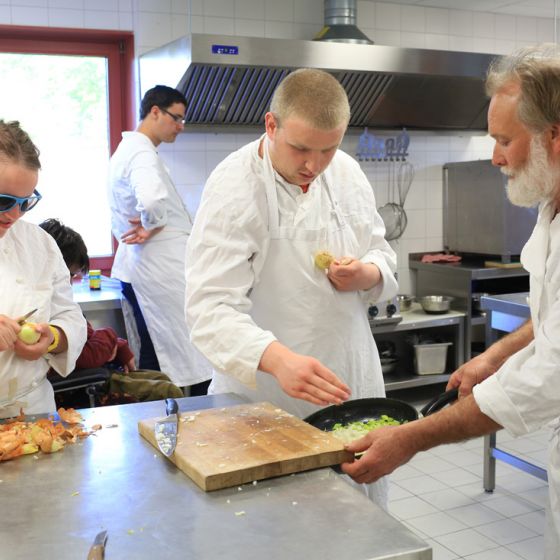 Koch und Schüler in der Schulküche beim Schneiden und Kochen