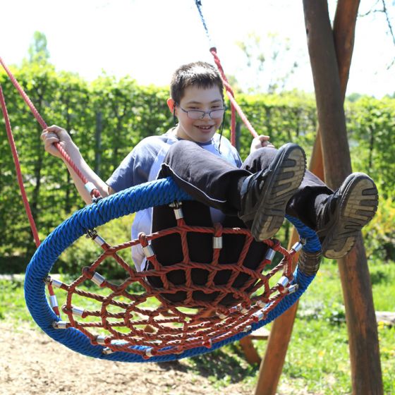 Ein Schüler mit Brille schaukelt lächelnd auf einer Schaukel in unserem Schulhof