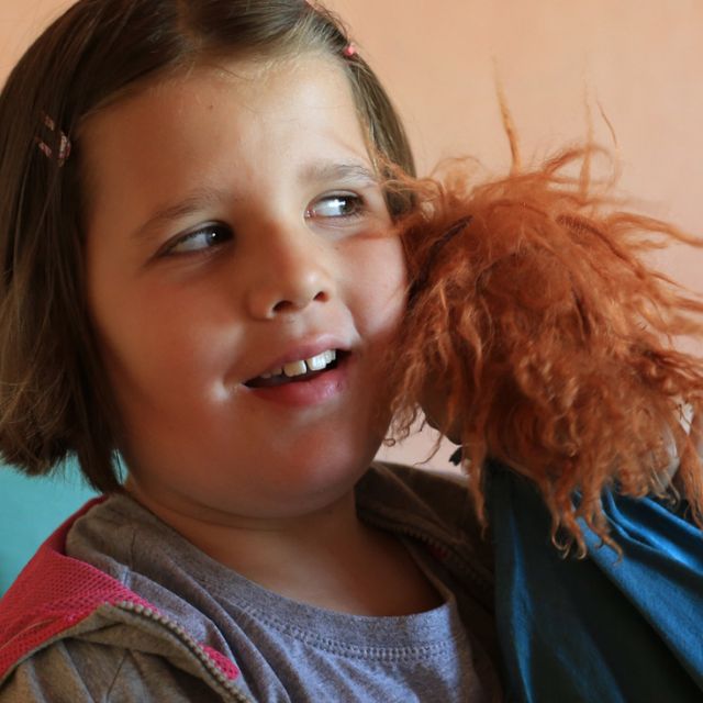 Ein Mädchen drückt eine rothaarige Handpuppe an sich und lächelt (vermutlich) ihre Lehrerin an