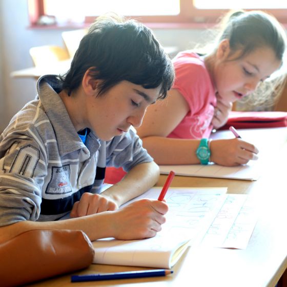 Junge und Mädchen schreiben in ihren Schulheften im hellen Klassenzimmer