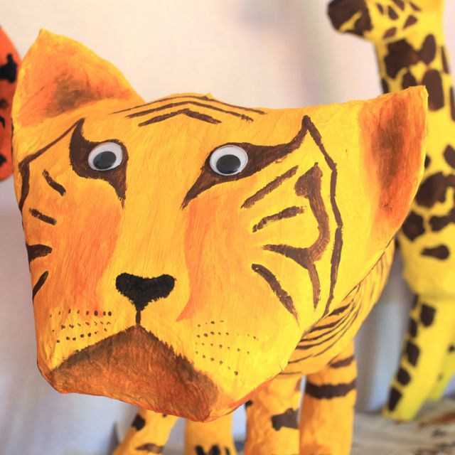 Kunstwerke aus Pappmaché: ein gelber Tiger schaut in die Kamera