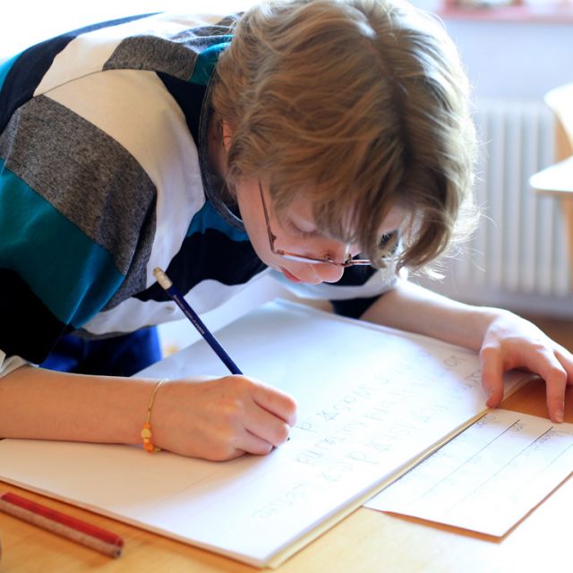 Eine Schülerin schreibt stehend in ihrem Heft und ist ganz vertieft darin