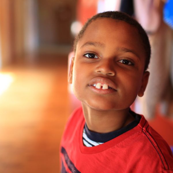 Ein dunkelhäutiger Junge im roten Shirt schaut in die Kamera, im Flur der Schule stehend